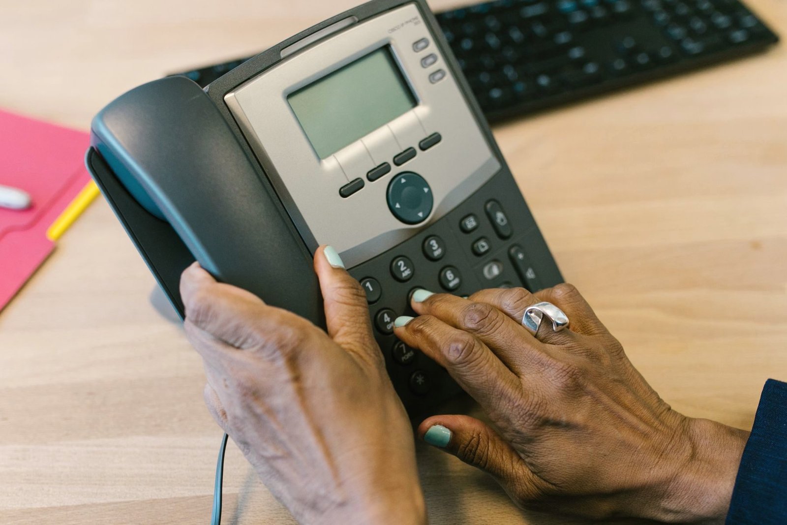 A hand presses the keypad of a multi-line desk telephone.