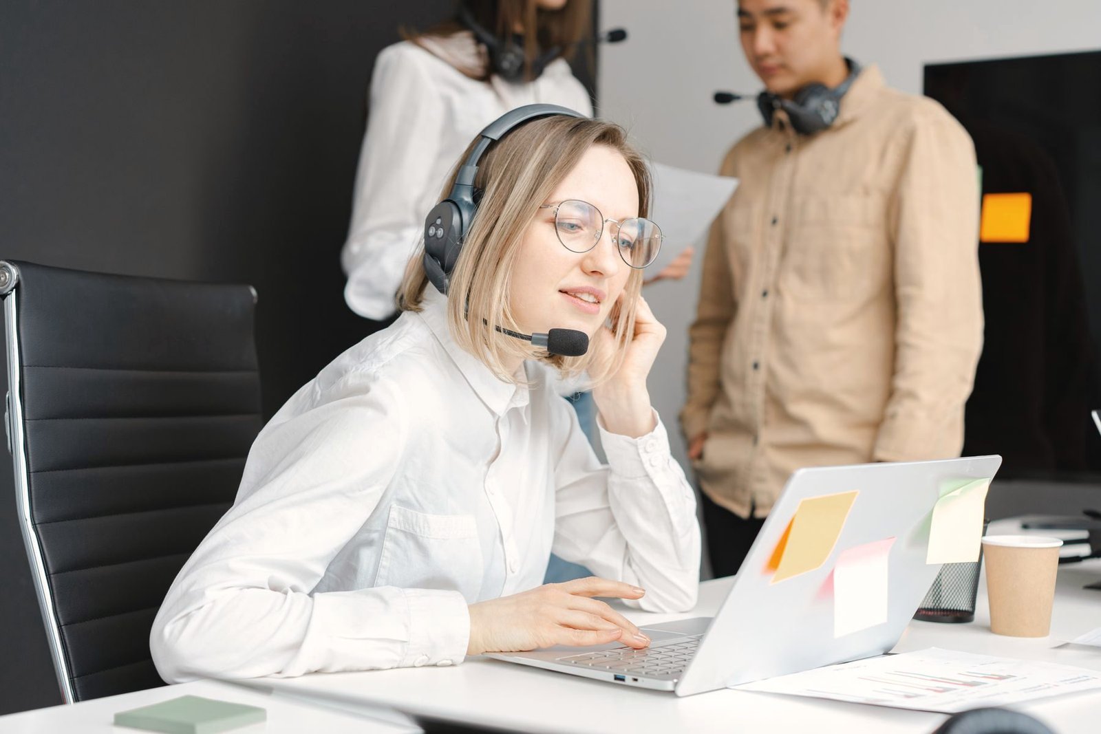 Two operators share a desk, each on a headset at a laptop.