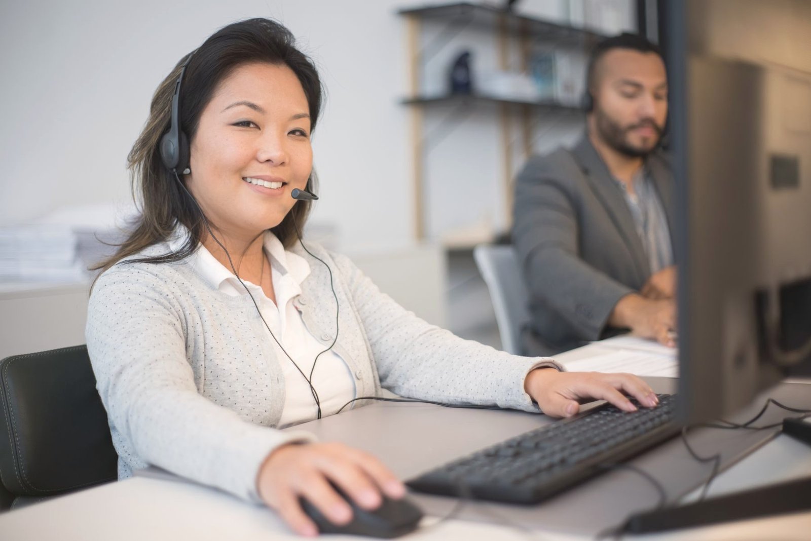 Two operators in headsets work together at computers in an office.