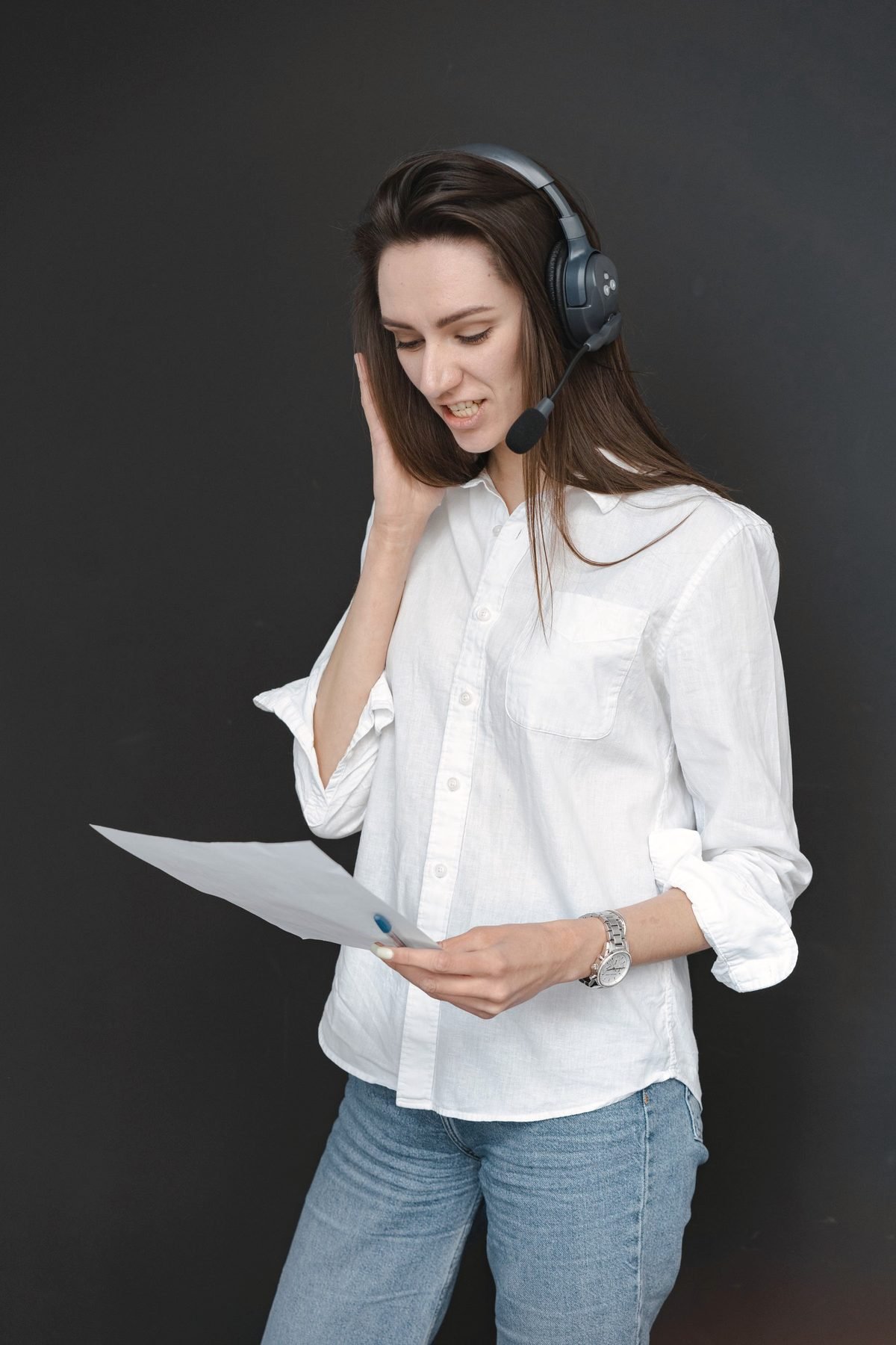 An operator in a white shirt reads a note aloud while taking a call on a headset.